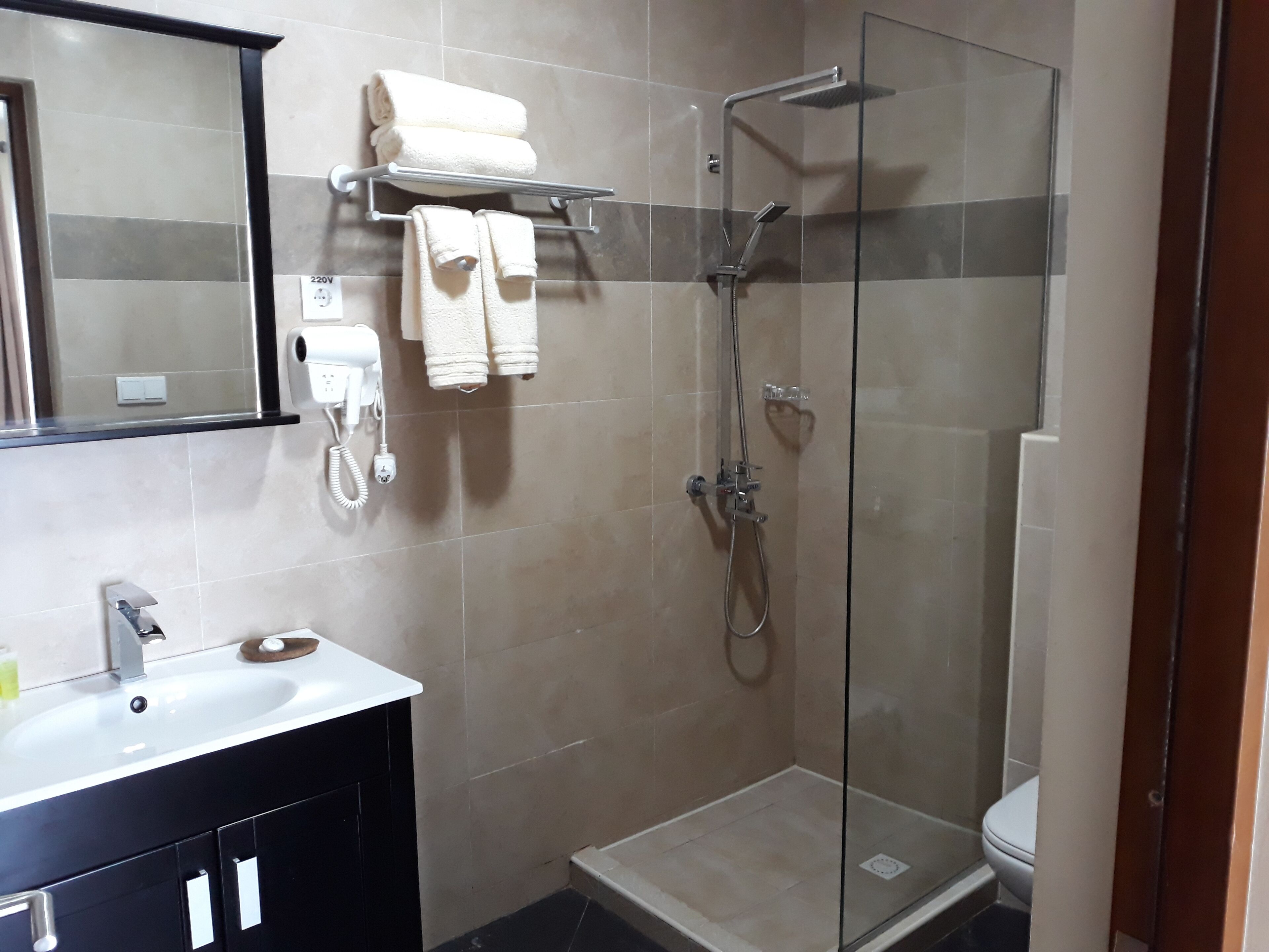 Ein modernes Badezimmer mit einer gläsernen Duschkabine, einem weißen Waschbecken und einer schwarzen Waschtischunterschrank.