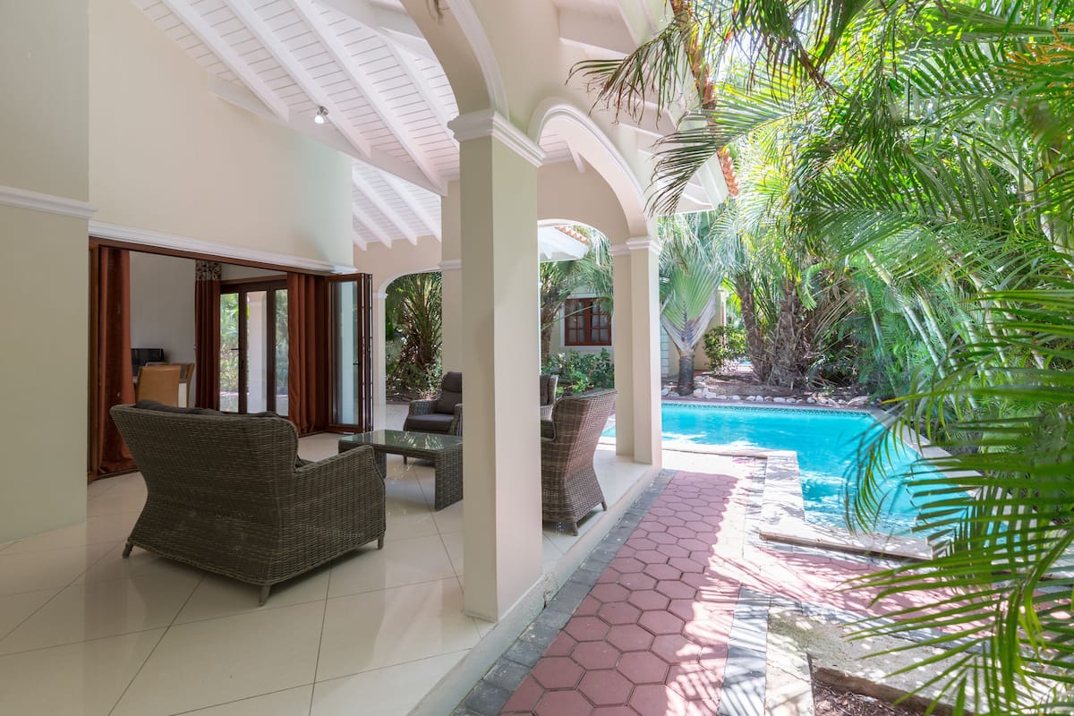 A covered outdoor area with a pool, wicker furniture, and a tiled floor.