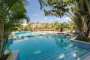 En swimmingpool med kristallklart blått vatten, omgiven av palmer och solstolar.