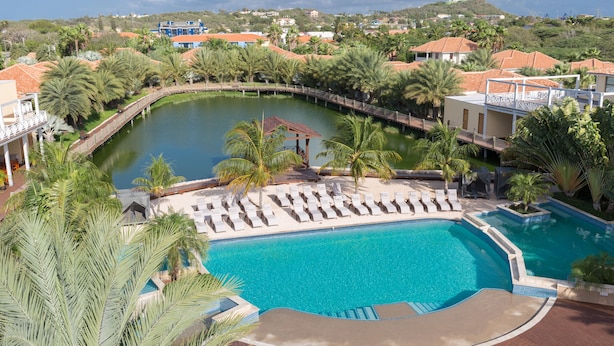 Un resort con una gran piscina, sillas de descanso, palmeras y vistas del paisaje circundante.
