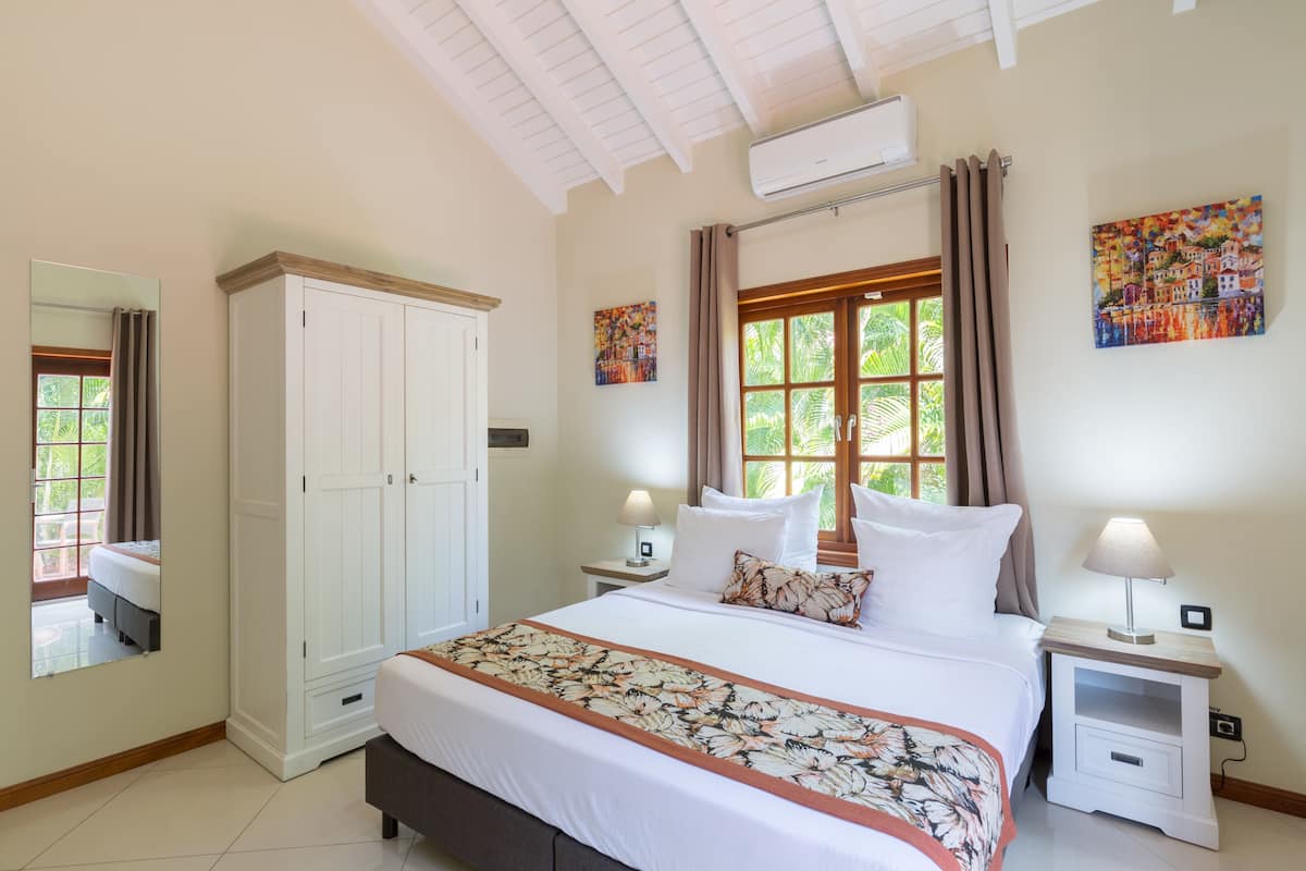 A bedroom with a large bed, a wardrobe, a nightstand, and a window with curtains.