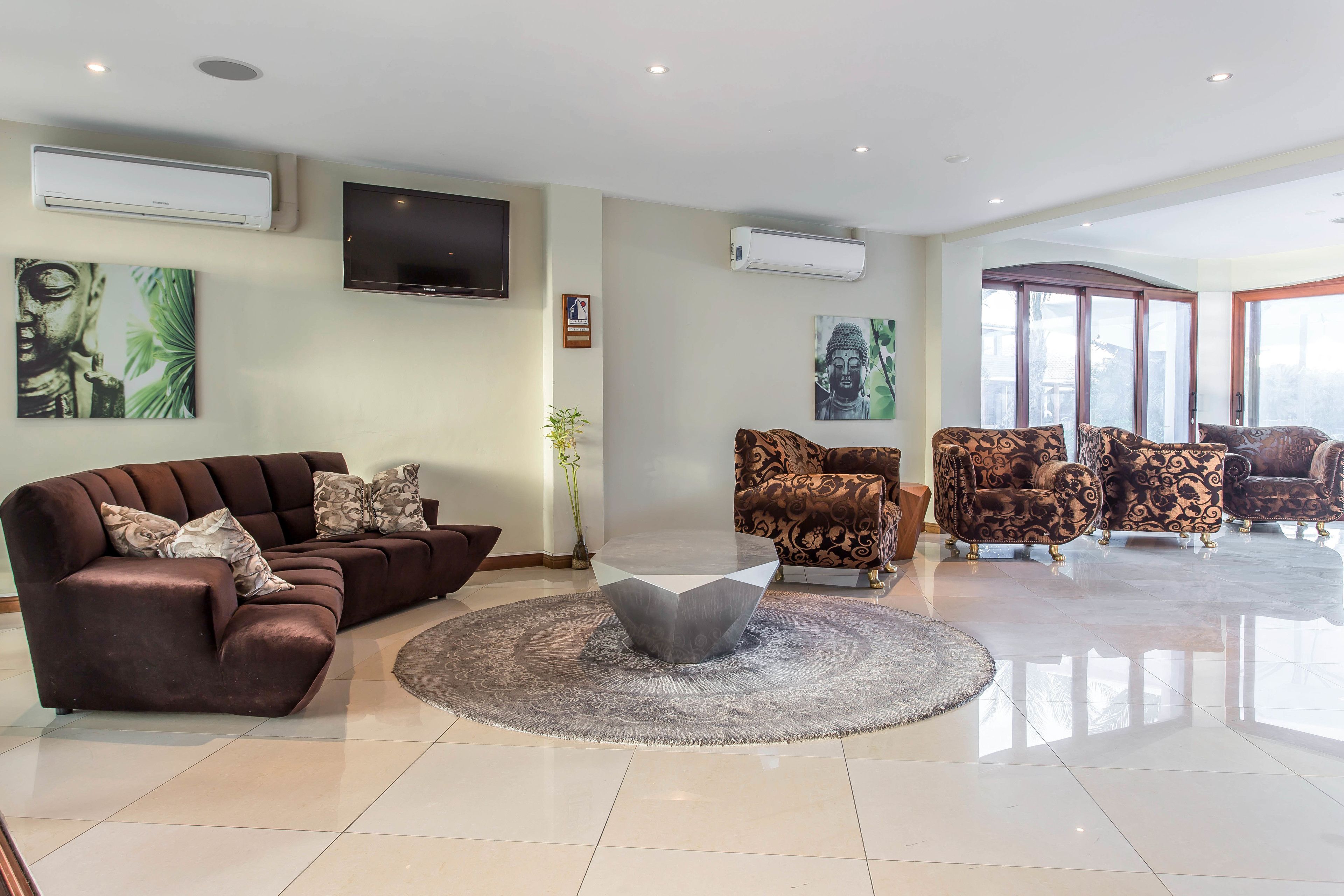 A spacious living room with a brown sofa, patterned armchairs, a central coffee table, and artwork on the walls.