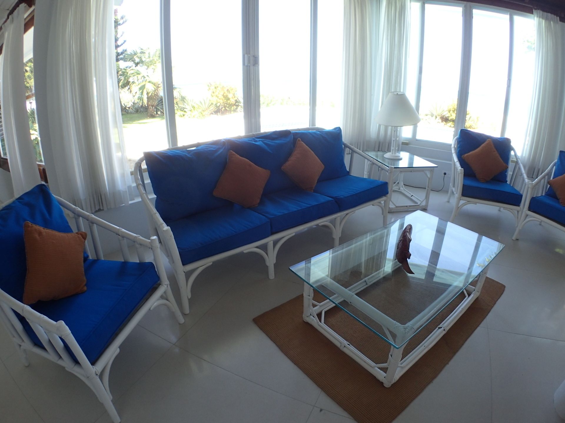 Une pièce comprenant un canapé bleu, des fauteuils blancs, une table basse en verre et une lampe.