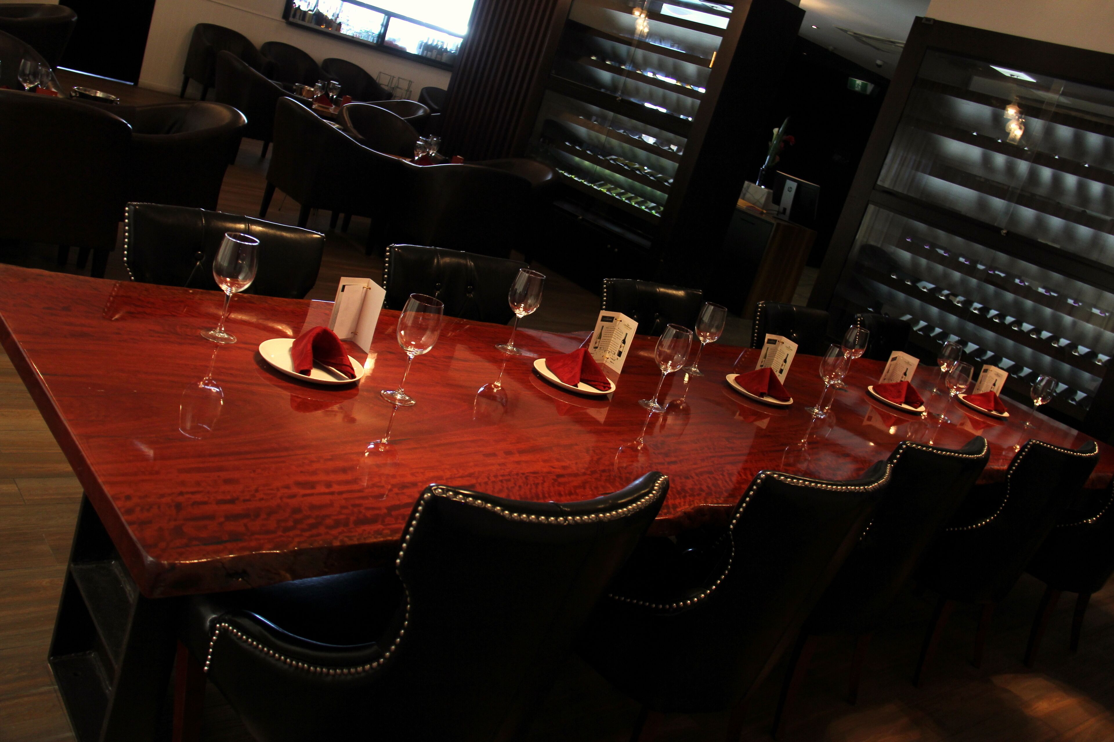 A dining area with a long wooden table set for multiple guests, surrounded by black upholstered chairs.