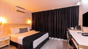 Una habitación de hotel con cama, mesita de noche, escritorio, silla y unidad de aire acondicionado.