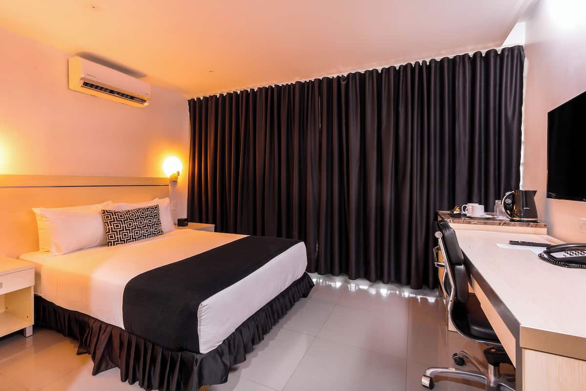 Habitació d'hotel amb llit, taulell de nit, escriptori, cadira i aire condicionat.