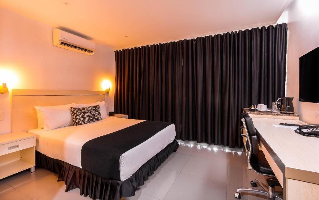 Habitación de hotel con una cama, un escritorio, una silla, un aire acondicionado y un televisor.