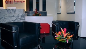 Zona de recepción de hotel con un mostrador de mármol, asientos de cuero negro y una silla de acento roja.