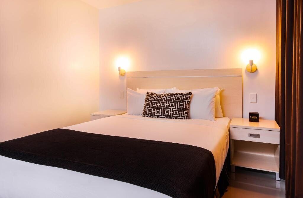 A hotel room with a bed, two bedside tables, a nightstand, and wall-mounted lamps.