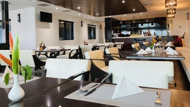 Un restaurante moderno con mesas dispuestas para comer, una zona de bar y una cocina visible al fondo.