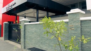 Una entrada de hotel con un toldo negro, una pared roja y una pared de piedra verde.