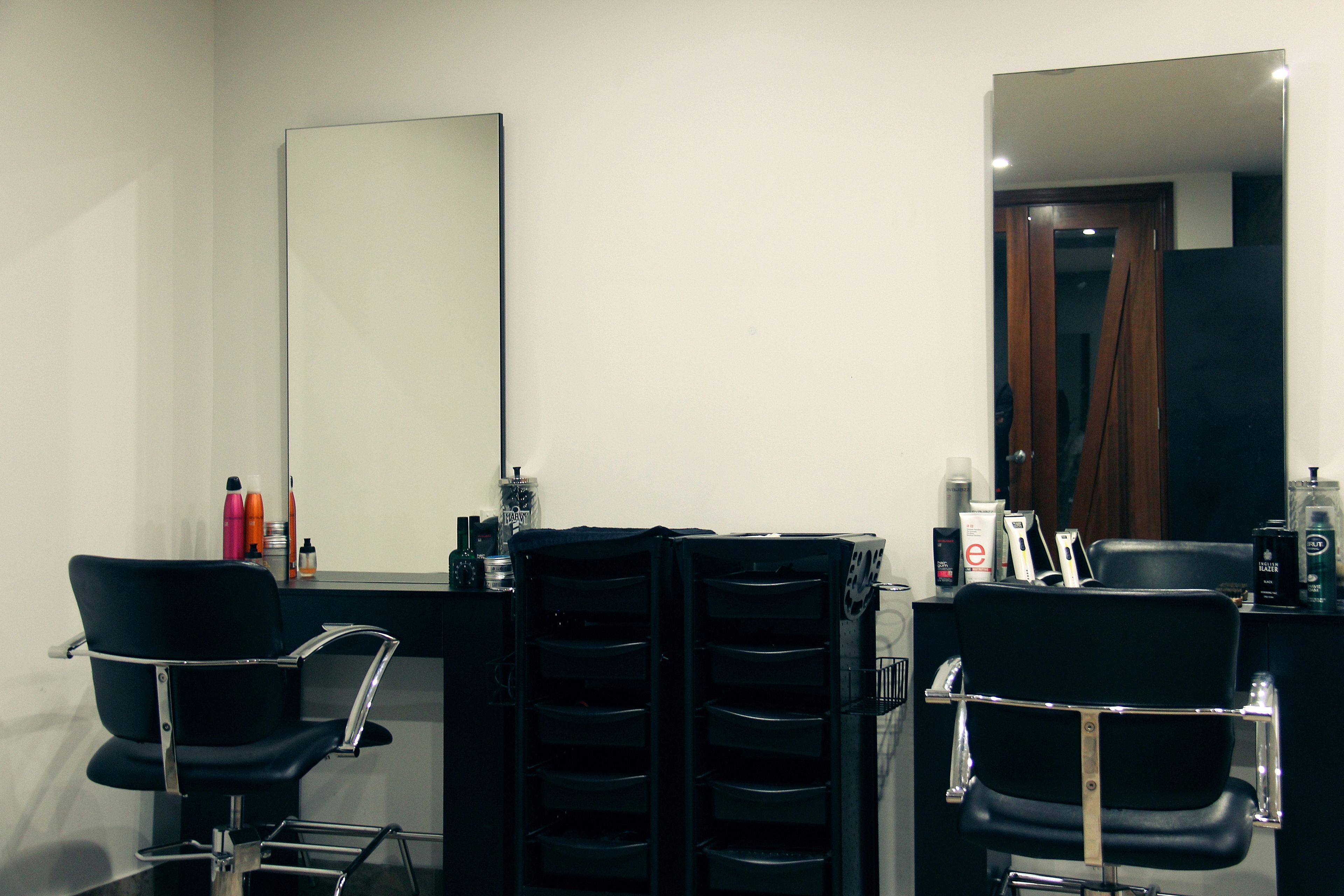 Ein moderner Friseursalon mit zwei schwarzen Friseurstühlen, einem großen Spiegel und verschiedenen Haarpflegeprodukten auf der Theke.