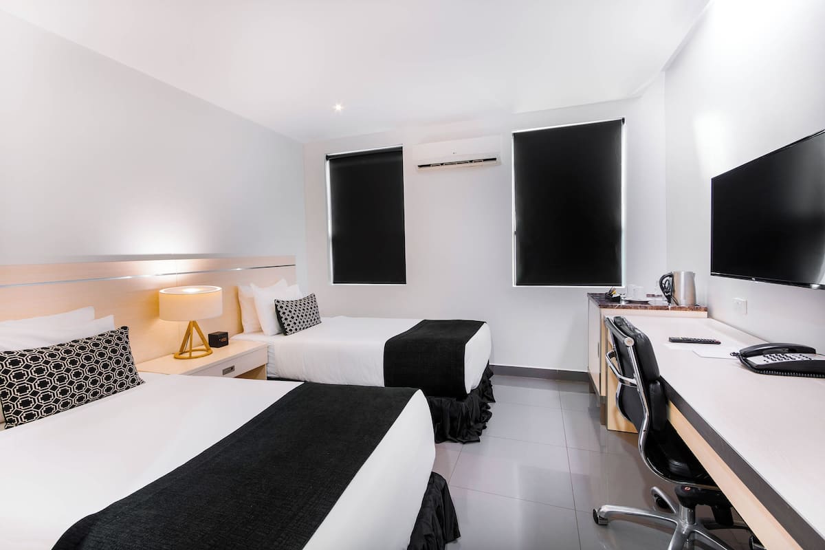 Una habitació d'hotel amb dos llits, una taula de treball, una cadira, un televisor i una màquina de cafè.