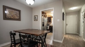 A dining area with a wooden table and chairs, a kitchen in the background, and a hallway leading to a door. - Less than 2 miles to Downtown and sleeps 6.  (Athens)