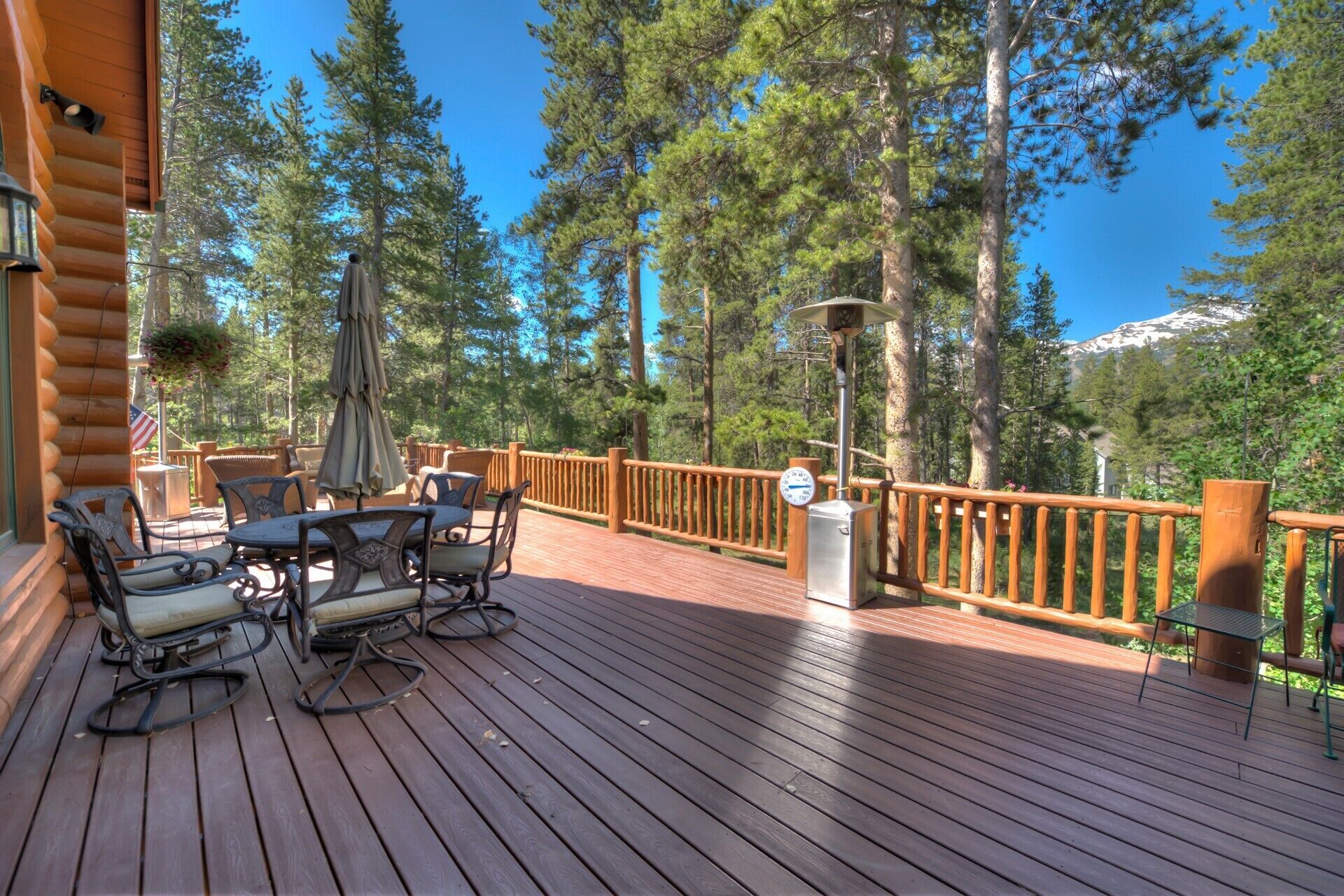 A wooden deck with outdoor furniture, a metal railing, and a view of trees and mountains.
