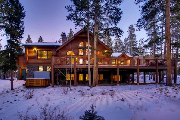 A log cabin with a balcony, surrounded by tall trees and snow.