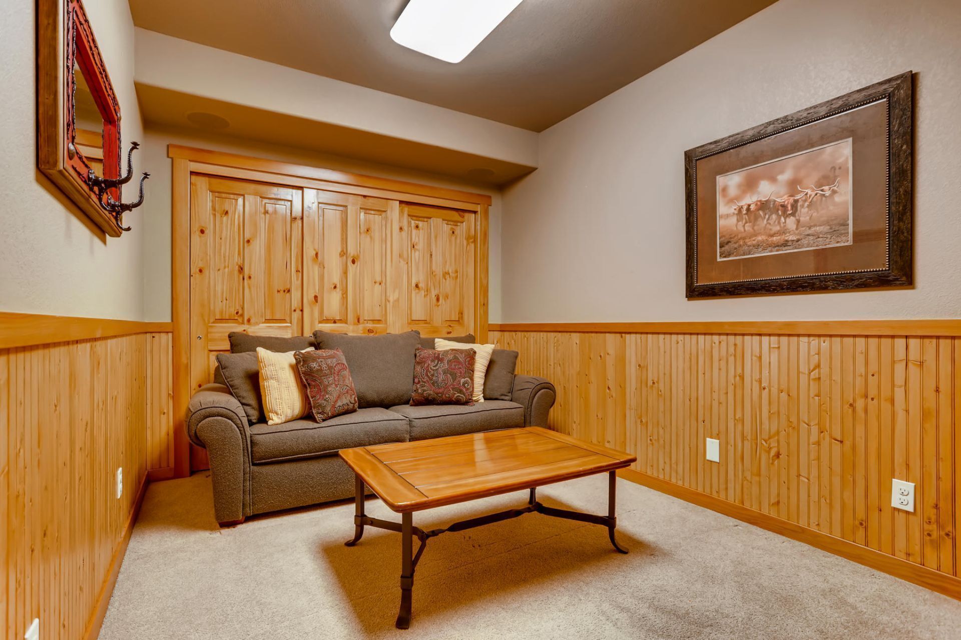 A room with a wooden paneled wall, a gray sofa with patterned cushions, a wooden coffee table, and a framed picture on the wall.
