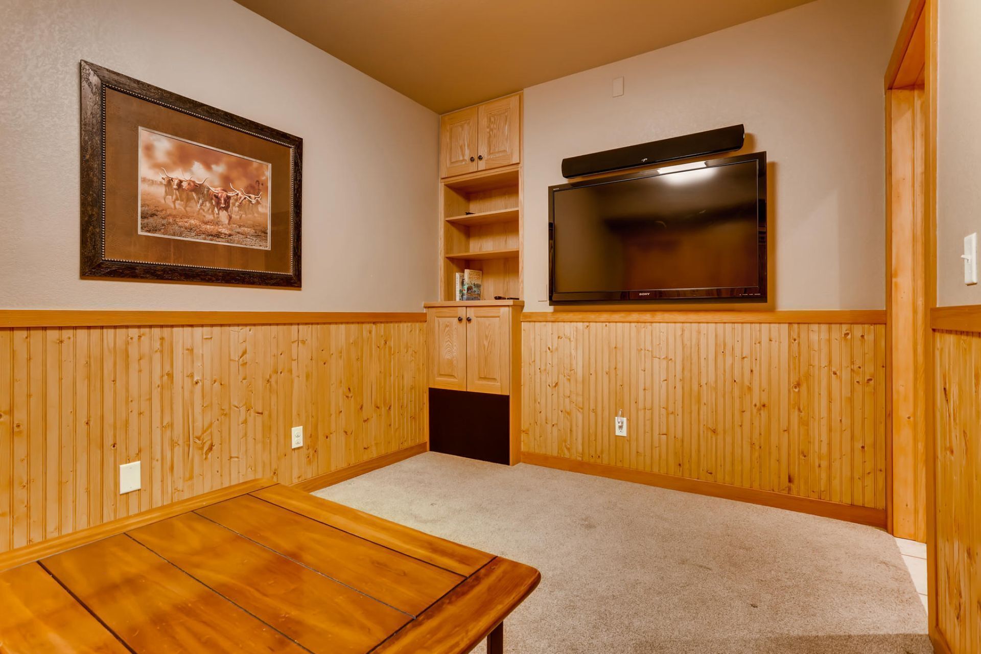 Une pièce avec des boiseries, un tableau encadré, un téléviseur à écran plat et une table en bois.