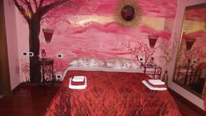Un dormitorio con una cama, una mesita de noche, un espejo y una pared decorada con un diseño de árboles y motivos florales.