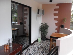 A small, compact room with a tiled floor, a wooden table, a chair, a potted plant, and a sliding door leading to another area. - Vali-Joe Travel Lodge (El Nido)