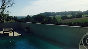 A dining table with a plate of toast and a glass of orange juice, a cup of coffee, and a view of a swimming pool and hills in the background. - Pretty Farmhouse / Private pool / 4 Doubles with en-suites & 1 Twin  / Sleeps 10 (Saint-Séverin)