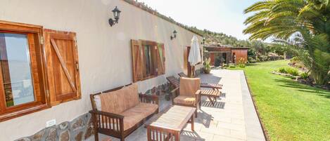 An outdoor patio with wooden furniture, stone flooring, and a well-maintained lawn.
