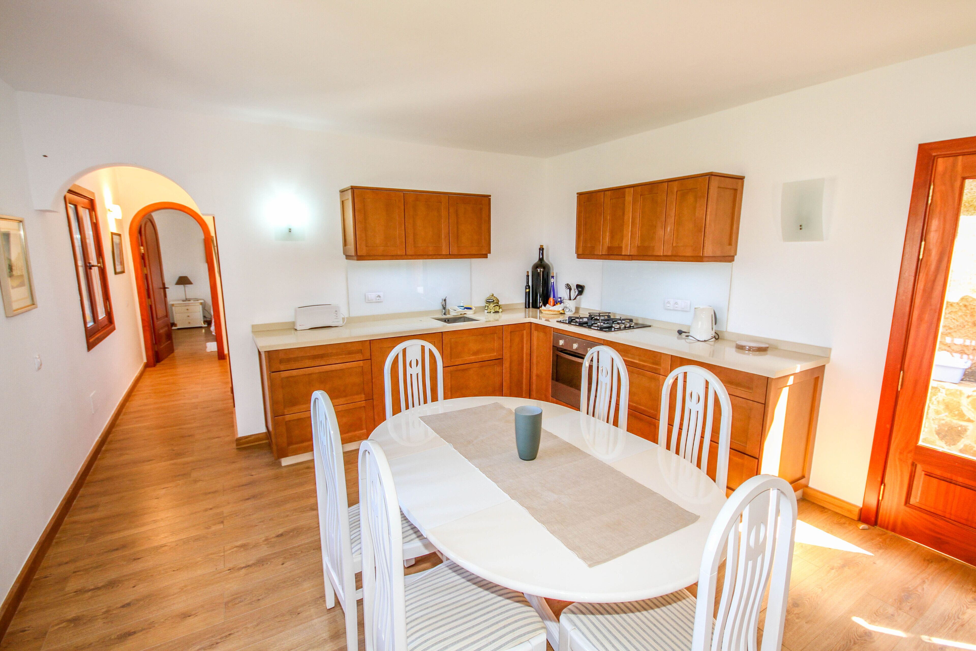 A modern kitchen with wooden cabinets, a dining table with chairs, and a view of the outside.