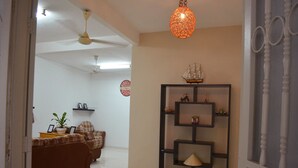 A living room with a brown sofa, a small table with a potted plant, and a decorative ship model on a shelf. - Gen-Ji Cottage (Malacca City)