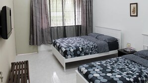 A bedroom with two beds, a window with curtains, an air conditioner, a wall-mounted TV, and a small bedside table with a bottle. - Gen-Ji Cottage (Malacca City)