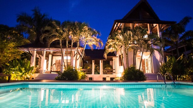 A resort pool area with a clear view of the pool, palm trees, and a building with a triangular roof. - Luxury villa, private beach, infinity pool. Fully serviced. Beautiful sunsets (koh chang)