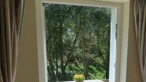 An open sliding door leading to an outdoor deck with a wooden table and chairs, a potted plant, and a view of a wooded area. - The Old Shippon, Crackington Haven, Bude, Cornwall, walk to the Beach Pub. (Crackington Haven)