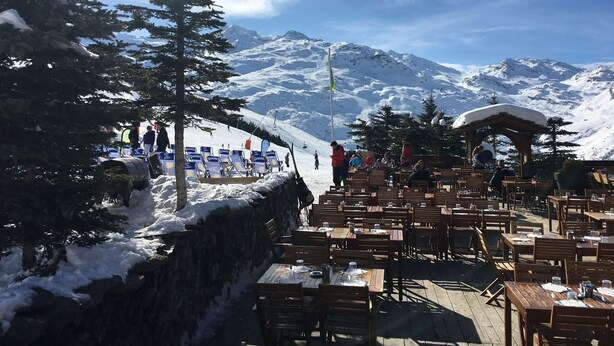 A snow-covered outdoor dining area with wooden tables and benches, set against a backdrop of snow-capped mountains and a clear sky. - luxury apartment at the foot of the slopes, indoor pool.  (Les Belleville)