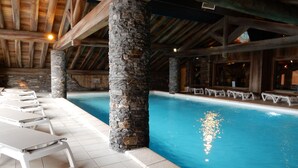 An indoor swimming pool with stone pillars, tiled floor, and white lounge chairs. - luxury apartment at the foot of the slopes, indoor pool.  (Les Belleville)