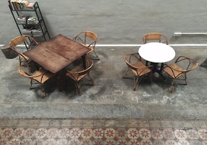 Un comedor con dos mesas, sillas de mimbre y una estantería con revistas.