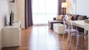 A modern living room with a sofa, a coffee table, and a dining area with chairs. - The Kannas Hotel (Chiang Mai)