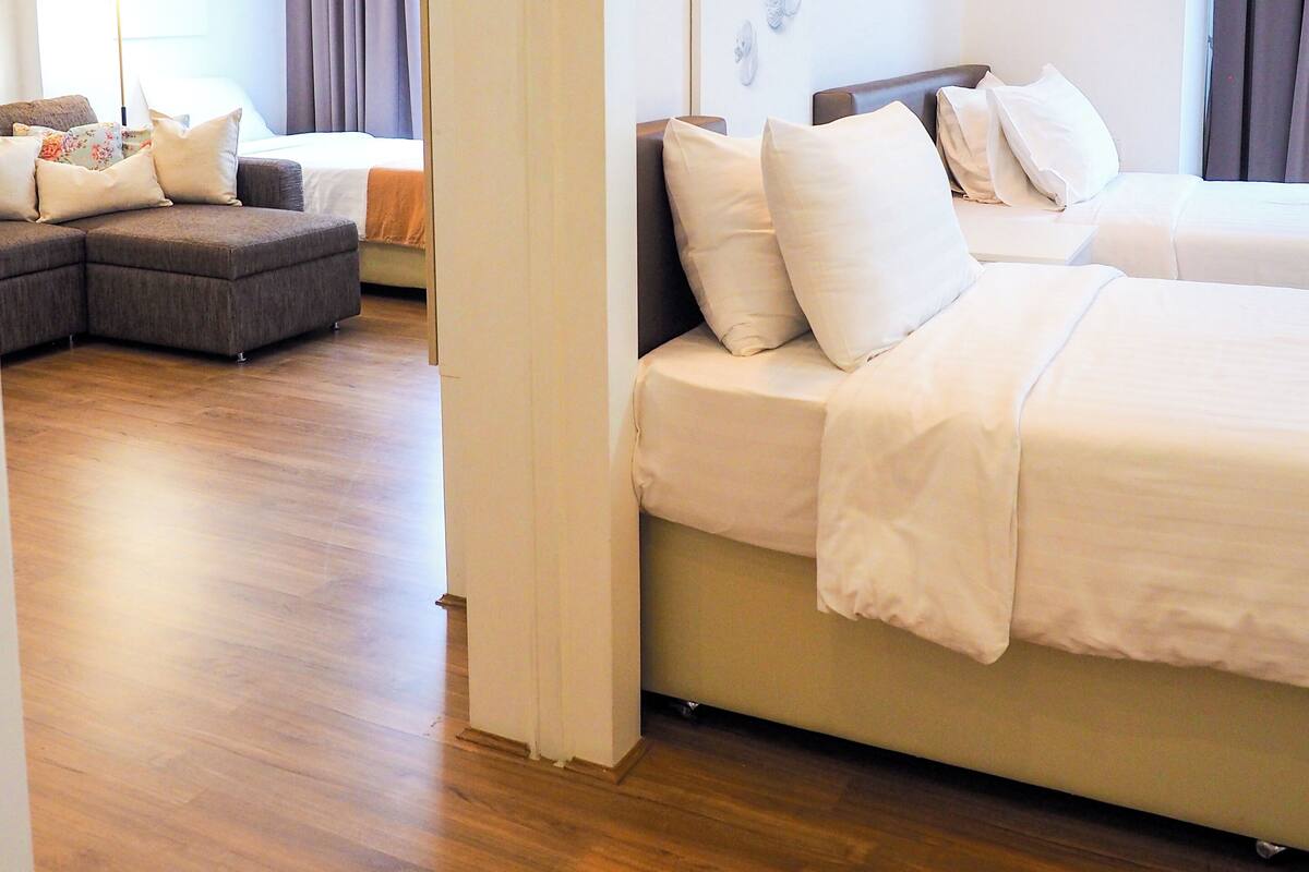 A hotel room with a large bed, a sofa, and a small table. There is a painting on the wall and a window with curtains.