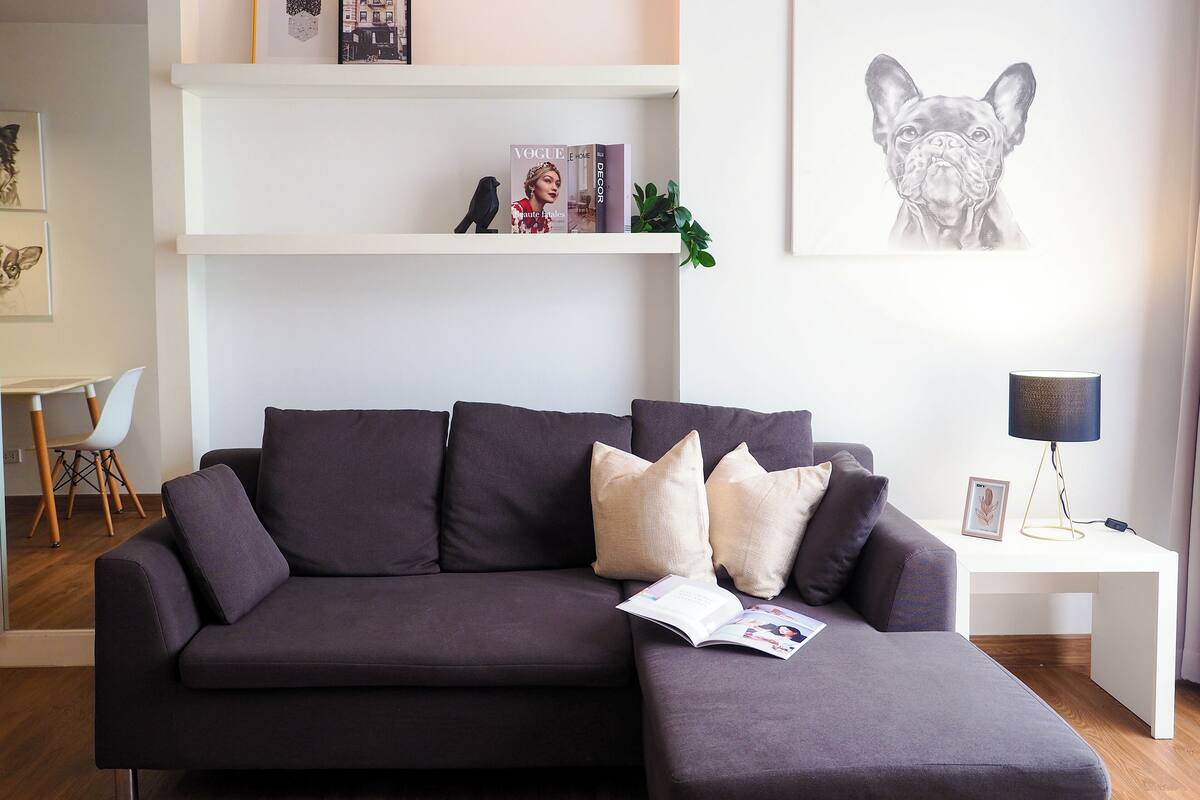 A modern living room with a dark grey sofa, multiple cushions, a magazine, and a framed picture on the wall.