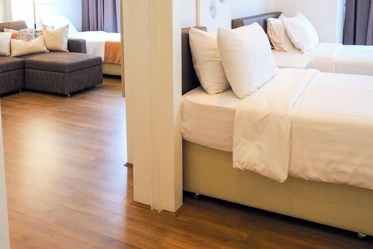 A hotel room with a bed, a sofa, a wooden floor, and a painting on the wall.