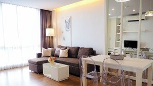 A modern living room with a sofa, coffee table, and dining area with chairs. - The Kannas Hotel (Chiang Mai)
