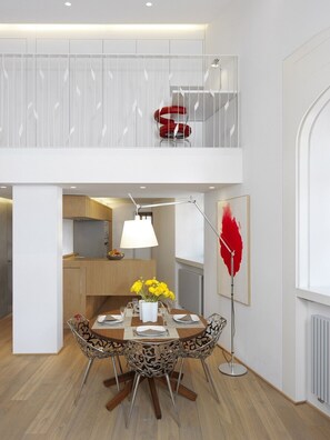 A modern dining area with a wooden table, metal chairs, a red chair on the upper level, and a floor lamp.