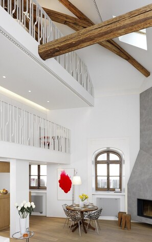 A spacious interior with a high ceiling, exposed wooden beams, a dining area with a table and chairs, and a fireplace.