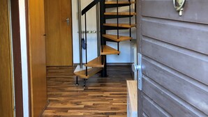 Eine Holztreppe mit Metallgeländer, eine Holztür mit einem Rauchverbotsschild und ein 'Willkommen'-Schild über der Tür.