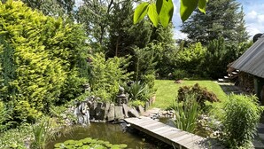 Ein friedlicher Garten mit Teich, einer Holzbrücke und üppigem Grün.