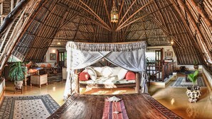 A thatched-roof room with a bed, wicker furniture, and a hanging lantern. - Large luxury beachside villa with a pool, guesthouse, cook, gardener, and maid (Diani Beach)