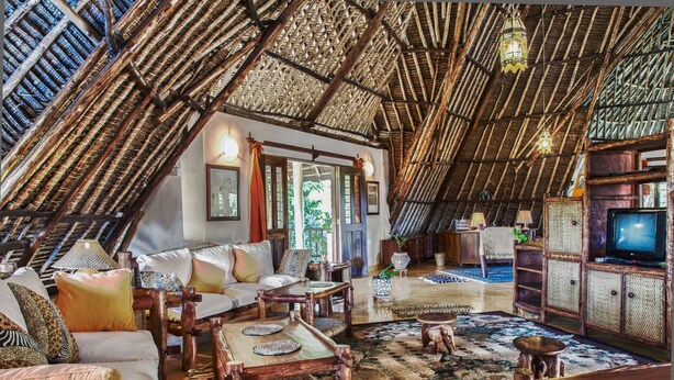 A spacious living area with a high thatched roof, comfortable seating, a television, and a large window providing natural light. - Large luxury beachside villa with a pool, guesthouse, cook, gardener, and maid (Diani Beach)