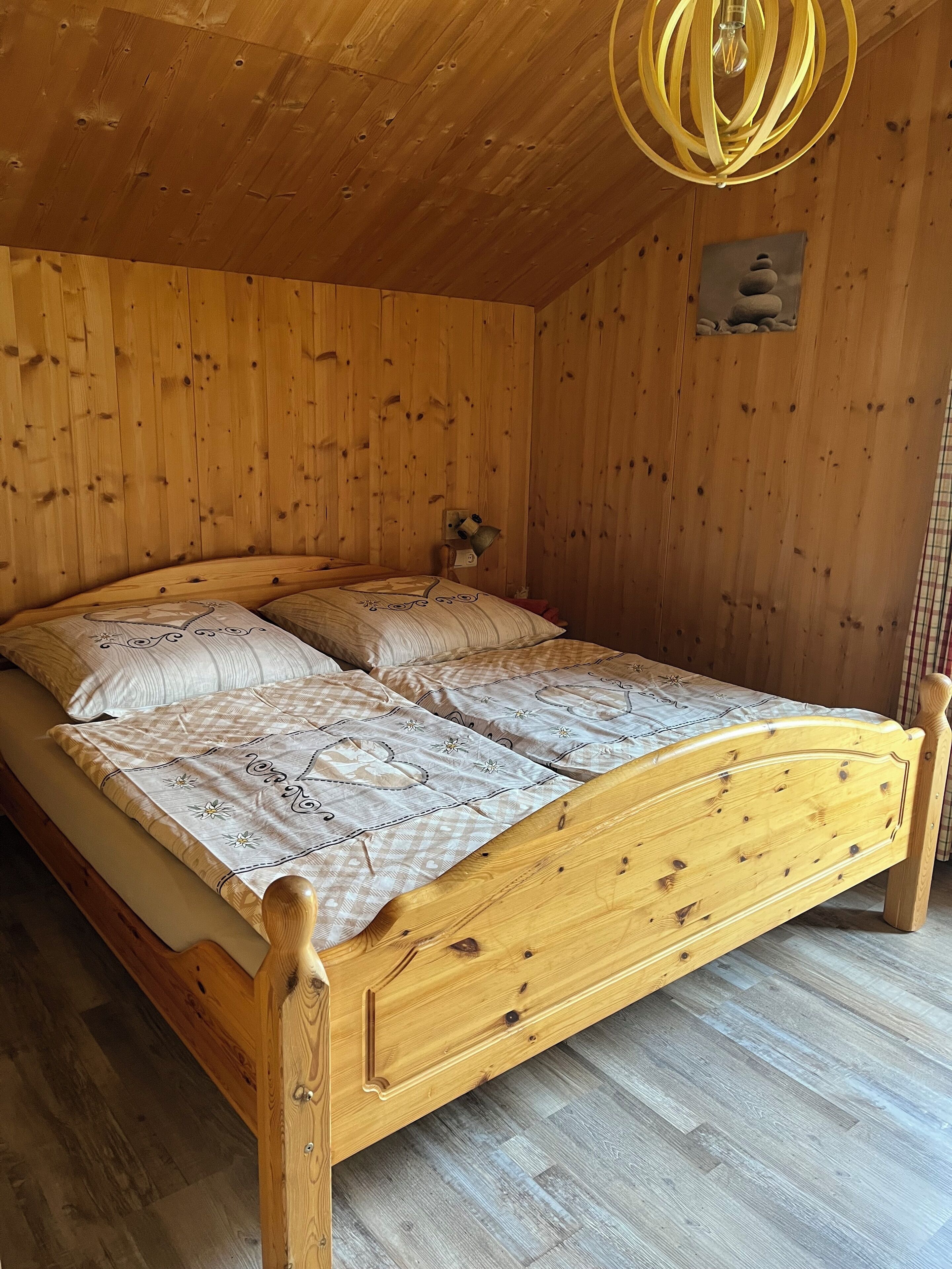 A wooden bed with a headboard, a wooden ceiling, and a wall-mounted light fixture.
