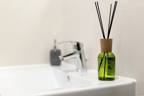 Un lavabo de salle de bain avec une bouteille en verre verte contenant des tiges de roseau.