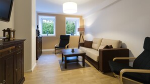 A living room with a sofa, two armchairs, a coffee table, a TV, a lamp, and a cabinet. - with underfloor heating and WiFi (Berlin)