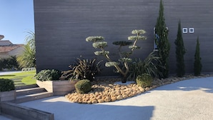 A modern building with a grey facade, a landscaped garden with various plants, and a gravel driveway. - Luxury villa with private pool 500m from the beach St Cyprien Porto Vecchio (Lecci)