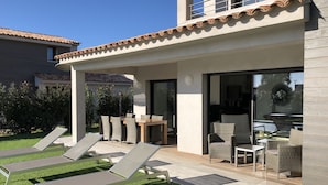 A modern house with a patio, outdoor furniture, and a glass door leading to a dining area. - Luxury villa with private pool 500m from the beach St Cyprien Porto Vecchio (Lecci)
